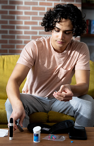 Teen boy sitting on couch using glucometer.