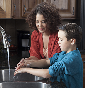 Woman helping boy wash hands in kitchen sink.