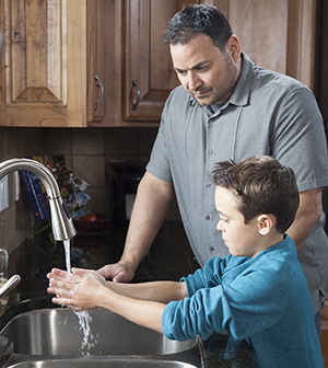 Man helping boy wash hands in kitchen sink.