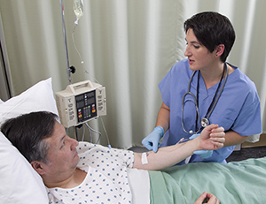 Man lying in hospital bed with IV in arm. Health care provider is checking IV.