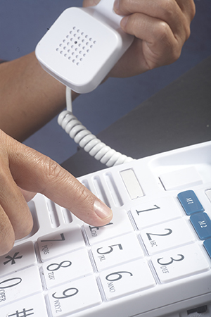 Closeup of hands dialing large-button telephone.