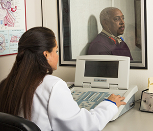 Audiologist performing hearing test on man sitting in booth.