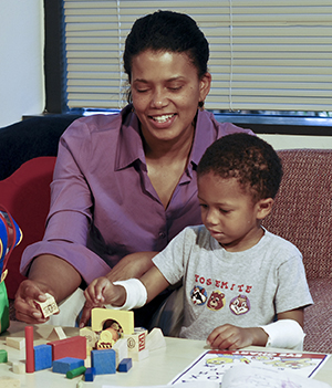 Woman watching boy play with blocks. Boy has gauze wrapped around both forearms.